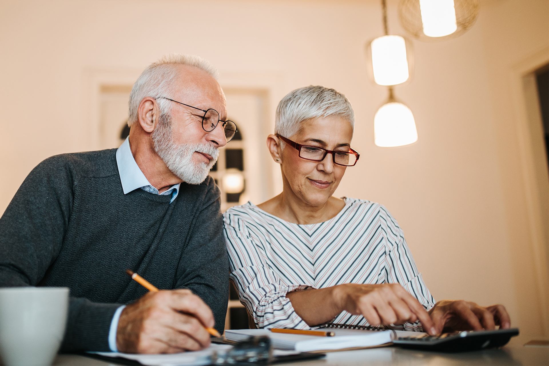 A senior heterosexual couple reviewing finances with a pencil, notepad, and calculator.