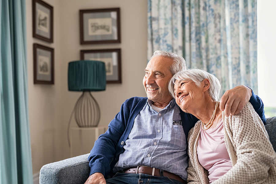 Older couple sitting on couch at home, smiling.
