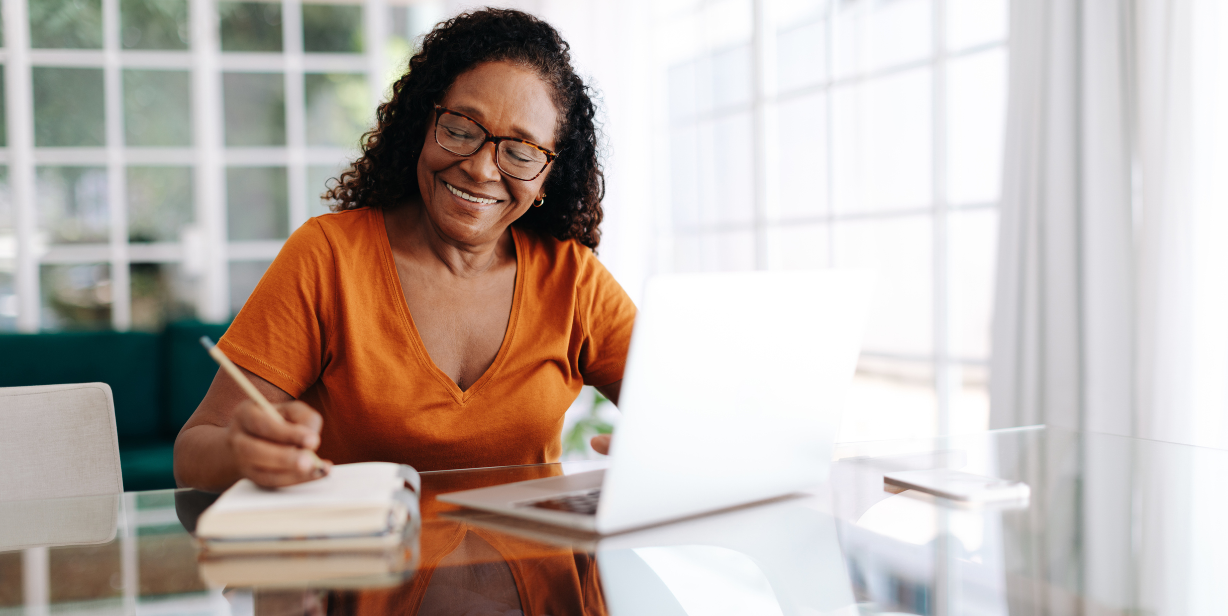 An older adult woman takes notes while on her laptop